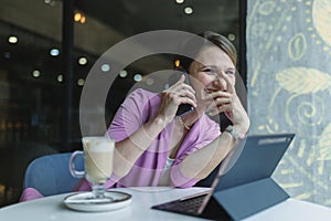 Young caucasian business woman laughing while talking on the phone while sitting in a cafe at a table during lunch