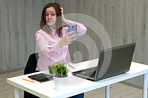 Young caucasian business woman in pink shirt in office doing selfie on the phone