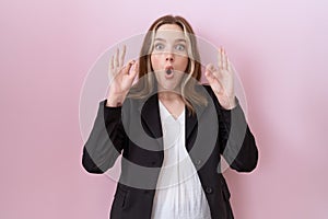 Young caucasian business woman wearing black jacket looking surprised and shocked doing ok approval symbol with fingers