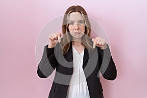 Young caucasian business woman wearing black jacket pointing down looking sad and upset, indicating direction with fingers,