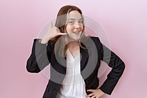 Young caucasian business woman wearing black jacket smiling doing phone gesture with hand and fingers like talking on the