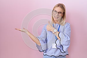 Young caucasian business woman wearing id card showing palm hand and doing ok gesture with thumbs up, smiling happy and cheerful