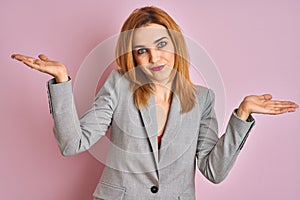 Young caucasian business woman wearing a suit over isolated pink background clueless and confused expression with arms and hands