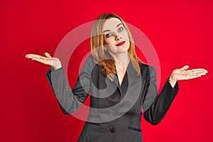 Young caucasian business woman wearing a suit over isolated red background clueless and confused expression with arms and hands