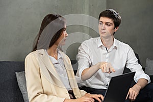 Young caucasian businessman and businesswoman serious look at together, working with computer together, man point to laptop. Young