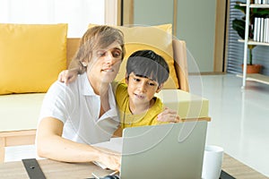 Young caucasian businessman and father working from home with notebook computer and taking care of little son in living room.