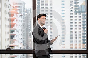 Young caucasian businessman holding necktie and tablet in modern office