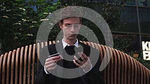 Young caucasian businessman outdoors on bench near modern office use mobile phone credit plastic card buying online