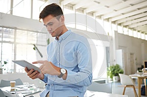 Young caucasian businessman working on a digital tablet alone in an office. One male boss holding and using social media