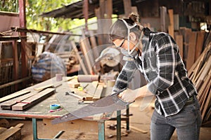 Young Caucasian carpenter man is sawing plank of wood in his own garage style workshop for hobby