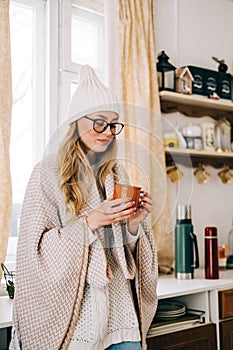 Young caucasian cheerful woman standing on a kitchen and drinking tea on winter morning