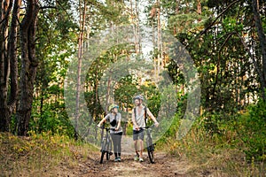 Young caucasian couple of cyclists walk and push their mountain bikes along the forest road in the park. Active sports weekend.