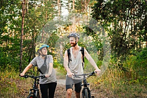 Young caucasian couple of cyclists walk and push their mountain bikes along the forest road in the park. Active sports weekend.