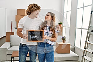 Young caucasian couple holding our new home blackboard hugging each other at new home