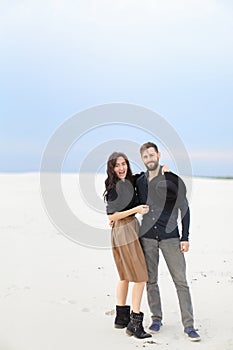 Young caucasian couple hugging in winter snow monophonic background, wearing skirt and black shirt.