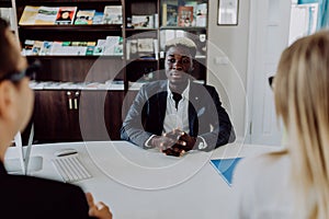 Young caucasian couple at meeting with african american man in formal wear talking at table in modern office