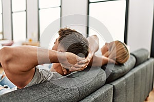 Young caucasian couple relaxing with hands on head sitting on the sofa at home