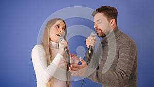 Young caucasian couple singing karaoke. Isolated on the blue background