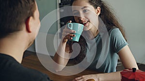 Young caucasian couple sitting at table in modern kitchen dicussing something in positive way, man is sitting back to