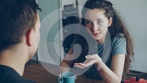 young caucasian couple sitting at table in modern kitchen dicussing something in positive way, man is sitting back to