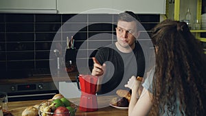 Young caucasian couple sitting at table in modern kitchen at home dicussing something, curly woman is sitting back to