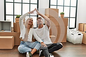 Young caucasian couple smiling happy doing house symbol with hands at new home