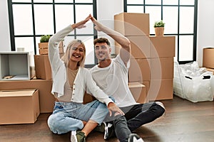 Young caucasian couple smiling happy doing house symbol with hands at new home