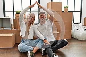 Young caucasian couple smiling happy doing house symbol with hands at new home