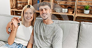 Young caucasian couple smiling happy holding key of new home sititng on the sofa