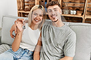 Young caucasian couple smiling happy holding key of new home sititng on the sofa