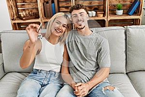 Young caucasian couple smiling happy holding key of new home sititng on the sofa