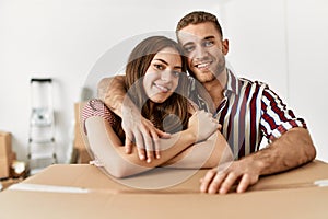 Young caucasian couple smiling happy leaning on cardboard box at new home