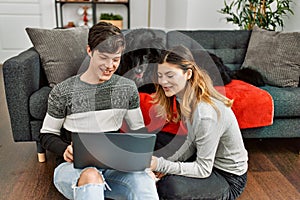 Young caucasian couple smiling happy using laptop sitting on the floor with dog at home