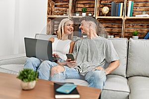 Young caucasian couple smiling happy using laptop and smartphone sitting on the sofa at home