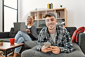Young caucasian couple smiling happy using laptop and smartphone sitting on the sofa at home