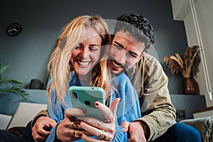 Young caucasian couple smiling using a cellphone to do shopping online. Man and woman watching the social media with a