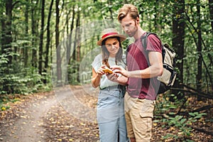 Young caucasian couple uses a smartphone to navigate in the forest. Hiking tourists orientation on the terrain using an online map