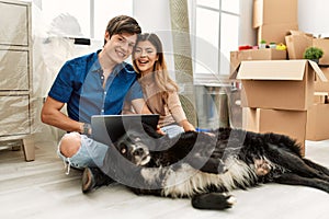 Young caucasian couple using laptop sitting on the floor with dog at new home