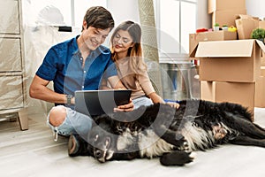 Young caucasian couple using laptop sitting on the floor with dog at new home