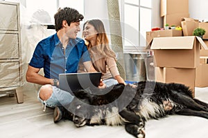 Young caucasian couple using laptop sitting on the floor with dog at new home