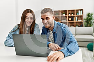 Young caucasian couple working using computer laptop at home looking positive and happy standing and smiling with a confident