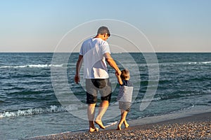 Young Caucasian dad with little son walk warm summer day along the sea coast. Summer family vacation concept. Friendship father