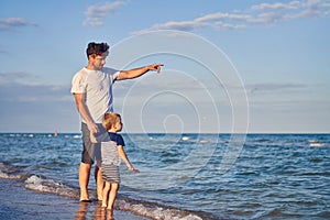 Young Caucasian dad with little son walk warm summer day along the sea coast. Summer family vacation concept. Friendship father