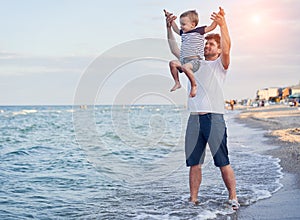 Young Caucasian dad with little son walk warm summer day along the sea coast. Summer family vacation concept. Friendship father