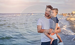 Young Caucasian dad with little son walk warm summer day along the sea coast. Summer family vacation concept. Friendship father