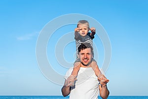 Young Caucasian dad with little son walk warm summer day along the sea coast. Summer family vacation concept. Friendship father