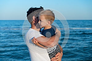 Young Caucasian dad with little son walk warm summer day along the sea coast. Summer family vacation concept. Friendship father