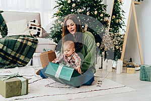 Young Caucasian diverse redhead mommy sitting on the floor with toddler unpacks Christmas present.