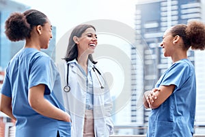 Young caucasian doctor in a lab coat standing outside and talking to mixed race nurses in scrubs. Diverse group of