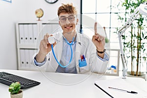 Young caucasian doctor man wearing doctor uniform and using stethoscope at the clinic smiling with an idea or question pointing